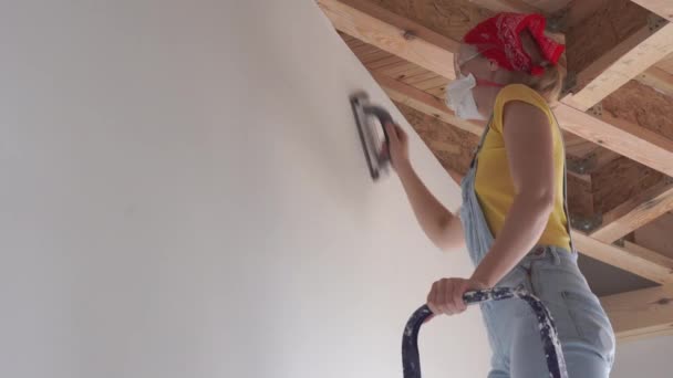 Reparatie in het appartement-een jonge vrouw van de Europese uitstraling maakt reparaties thuis-wandoppervlak polijsten — Stockvideo