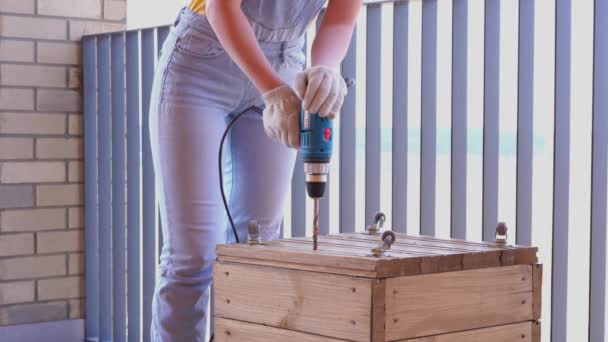 Una mujer en una terraza hace un trabajo no femenino - taladra un agujero con un destornillador en una caja de madera — Vídeos de Stock
