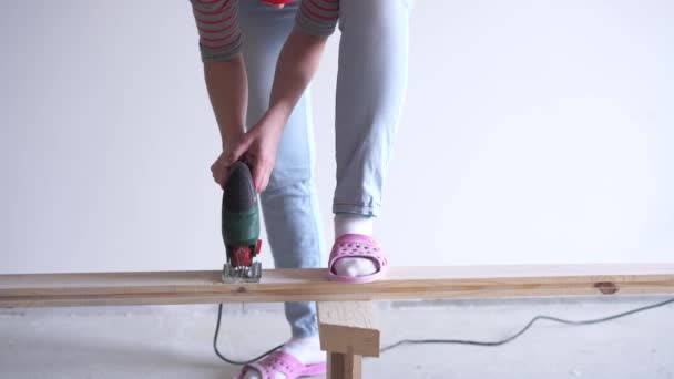 Una mujer hace un trabajo no femenino - aserrar una tabla de madera con un rompecabezas eléctrico — Vídeos de Stock