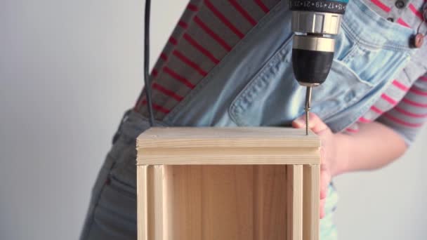 Женщина выполняет неженскую работу - сверлит отверстие с отверткой в деревянной коробке, замедленное движение — стоковое видео