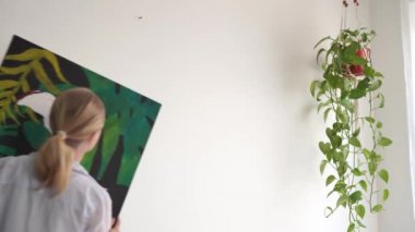 Yeni bir eve taşınıyorum. Genç sarışın bir kadın bir odada tuval üzerine bir resim döşeme.