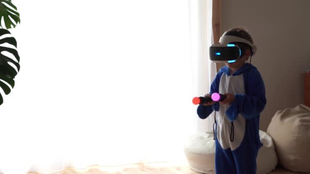 Современная жизнь молодежи. Новейшие электронные технологии в повседневной жизни. маленький мальчик играет дома в шлеме виртуальной реальности — стоковое видео