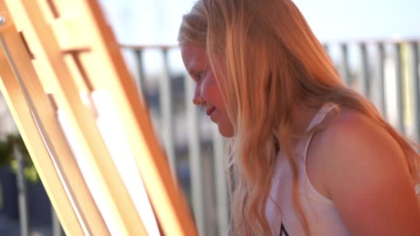 Hermosa rubia adolescente pinta un cuadro en la terraza — Vídeos de Stock