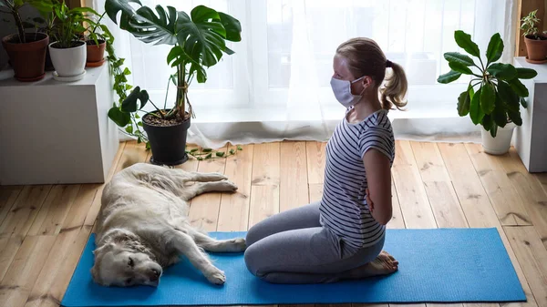 Stanna hemma. kvinna som gör yoga i vardagsrummet under karantän, en stor hund ligger i närheten. — Stockfoto