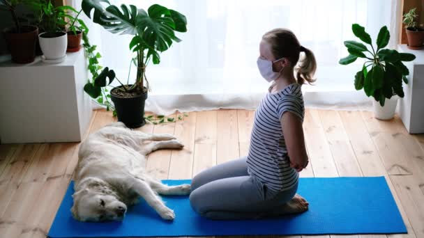 Blijf thuis. vrouw doet yoga in de woonkamer tijdens quarantaine, een grote hond ligt in de buurt. — Stockvideo