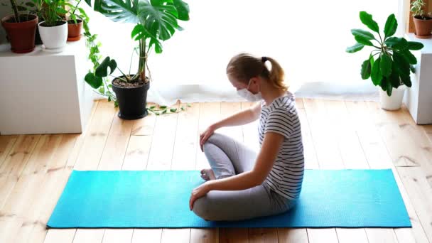 Stanna hemma. maskerad kvinna som gör yoga i vardagsrummet under karantänen — Stockvideo