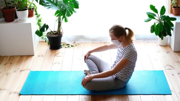 Stanna hemma. maskerad kvinna som gör yoga i vardagsrummet under karantänen — Stockvideo