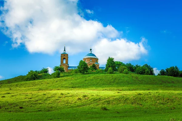 Traditionele Russische landschap - zomer met groene heuvels met gras op de achtergrond van de oude Russische kerk — Stockfoto