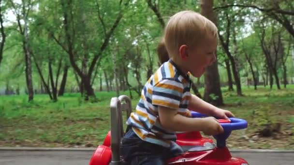 I ragazzini cavalcano sulle loro macchinine nel parco . — Video Stock