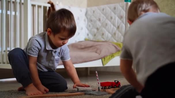 Barn leka med en träleksak, bygga en leksak-järnväg hemma. Barnen leker med tåg och bilar — Stockvideo