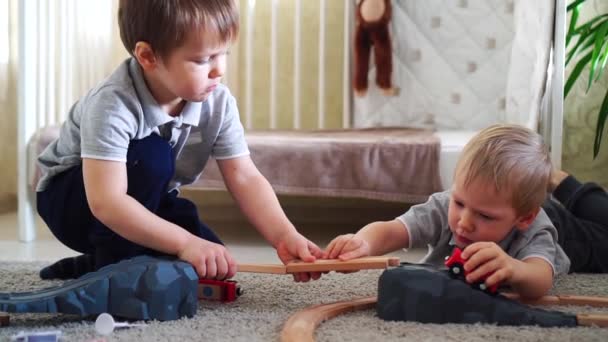 Діти грають з дерев'яним поїздом і будують іграшкову залізницю вдома — стокове відео