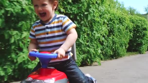 Счастливый маленький мальчик едет в парке на своей игрушечной машине — стоковое видео