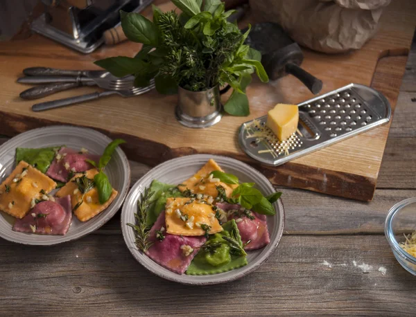 Op de houten tafel zijn grijze platen van ravioli pasta. Naast een heleboel kruiden, rasp met een stukje kaas en bestek. — Stockfoto