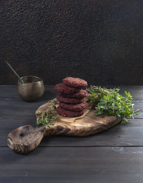 På ett svart träbord är en skärbräda med vegetariska kotletter och kryddiga örter. I närheten finns en koppar kastrull med en sked. — Stockfoto