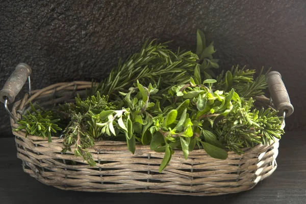 Auf einem schwarzen Holztisch liegt ein Weidenkorb mit würzigen Kräutern. — Stockfoto