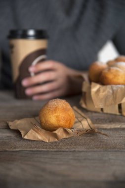 Üzerinde çöreklerle dolu bir sepet indiği masada, bir kız oturur ve bir bardak kahve tutar..