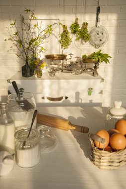 Provence tarzında güneşli natürmort. Vintage ölçekler ve vazolar beyaz tuğla duvarda göğüs üzerinde durmak. Baharatlı yeşillikler etrafında. Ön planda bir oklava ve hamur ingredien ile bir tablo