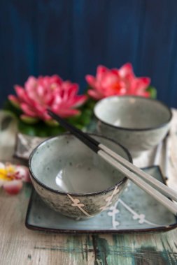 Eski ahşap masada Japon yemekleri için yemekler bir dizi. Nilüfer çiçeklerinin arkasında.