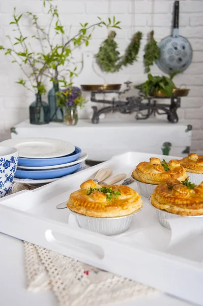 In de Provençaalse stijl keuken op de tafel is een dienblad met taarten. In de buurt zijn gerechten. Er is een kist bij de witte bakstenen muur. Op het zijn schalen en vazen met bloemen en greens. — Stockfoto