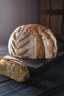 Bir kesim kenarı ile ev yapımı ekmek siyah ahşap bir masa üzerinde bir kesme tahtası üzerinde yatıyor. Güneş ışığı tabloyu aydınlatır.