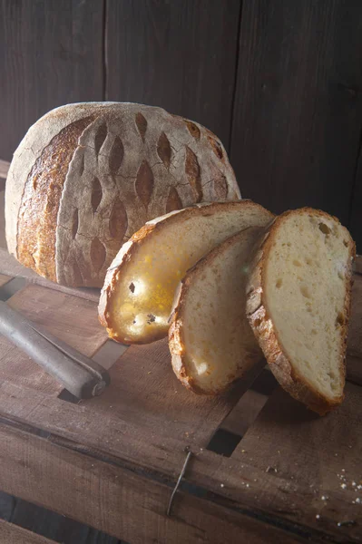 Güneş ışığı ev yapımı ekmek yarım somun ve dilimlenmiş ahşap kutu, aydınlatır. Sırada bir bıçak var.. — Stok fotoğraf