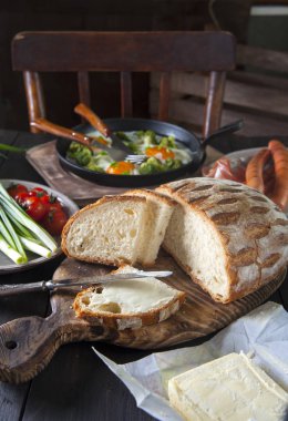 Kahvaltı siyah ahşap bir masaüzerine yatırılır: kızarmış yumurta, sosis, sebze ve tereyağı ile ev yapımı ekmek.