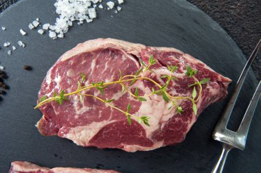 Sıcak yatıyor için gri bir stand üzerinde et, biftek ve tuz ve biber için bir çatal dağıtılır. Etin üzerinde kekik bir sprig olduğunu.