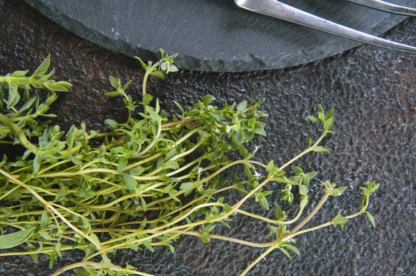 Auf einem braunen Metalltisch liegt ein Bündel Thymian. In der Nähe befindet sich ein grauer Glühständer und Besteck. — Stockfoto