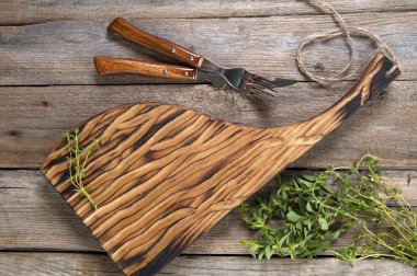 Ahşap bir yüzey üzerinde bir kesme tahtası ve çatal üzerinde yatıyor. Bir demet baharatlı otların yanında.