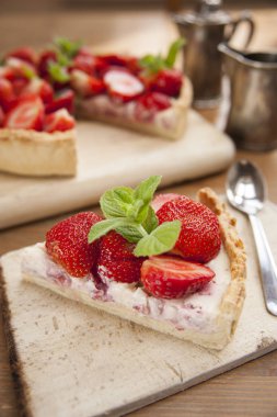 Masanın üst görünümü. Üzerinde bir dut turtası ve tahta bir platoda ayrı bir dilim yatıyor. Yakınlarda bir çay kaşığı ve gümüş kahve seti var..