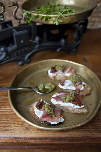 Sul vecchio tavolo c'è un piatto di rame con una bruschetta con crema di formaggio, pancetta e pomodori. Dietro ci sono scale antiche . — Foto Stock