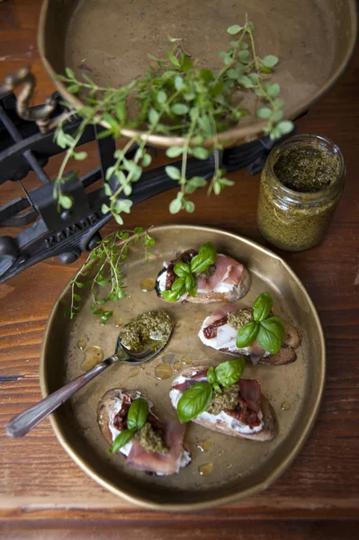 Vista dall'alto di un antico tavolo sul quale spicca una ciotola di rame con bruschetta con formaggio, pancetta, pomodori, pesto e basilico. Dietro ci sono scale antiche . — Foto Stock