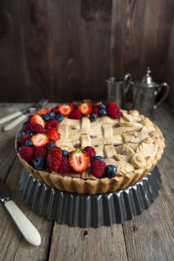 Ahşap bir masa üzerinde bir stand üzerinde çilek ile bir cupcake duruyor. Sola çatal bıçak takımı. Gümüş kahve demliği ve sütçü arkasında.