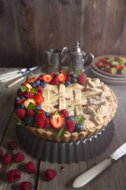 Güneş ışığı, ahşap bir masanın üzerinde duran taze meyvelerle süslenmiş bir dut çöreği aydınlatır. Çatal bıçak takımı serildi. Gümüş bir set ve çilek ile tabak arkasında.