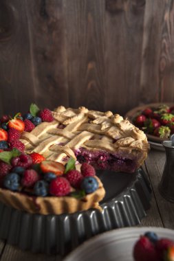 Taze çilek ile dekore edilmiş bir kesme berry muffin ahşap bir masa üzerinde bir stand üzerinde duruyor. Yakınlarda gümüş süt sürahisi var. Bir tabak çilekin arkasında.
