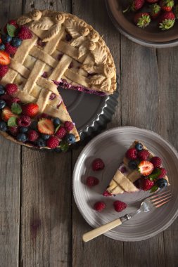 Taze ahududu ve çilek ile süslenmiş berry pasta bir dilim ile bir tabak duruyor ahşap bir masa üzerinde üst görünümü. Bir pasta ve çilek ile tabak yakınında.
