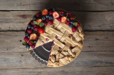 Taze ahududu ve çilek ile süslenmiş çentikli bir dut pasta bir stand üzerinde duruyor ahşap bir masanın üst görünümü. Close.