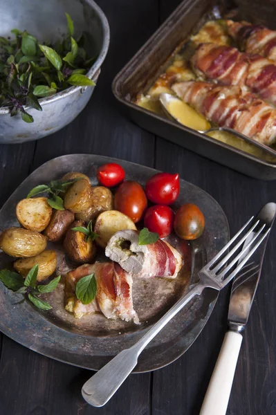Fekete fadobozon áll egy ezüstszínű tányér, hústekercsekkel és zöldségekkel. A közelben van evőeszközök, és mögötte van egy sütés-csészébe tekercs és egy szűrőedény zöld bazsalikommal. — Stock Fotó