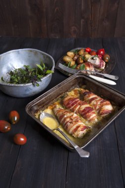 Sos ve bir kaşık pişmiş et rulo ile bir fırın yemeği siyah ahşap bir masa üzerindedir. Arkasında köfte ve sebze ve yeşil fesleğen ile bir kevgir ile gümüş bir tabak.