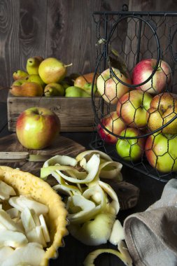 Pişirme için hazırlanan elma dolgulu bir pasta ile bir form masada. Yakındaki bir metal sepet ve sandık elma ve armut vardır.