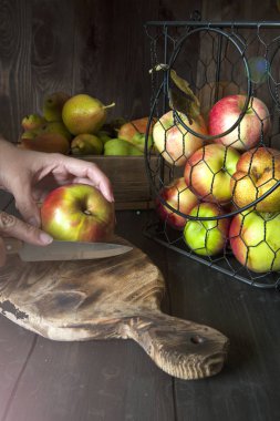 Olgun elma ve armut bir sepet ve siyah ahşap bir masa üzerinde bir kutu serilir. Bıçaklı kız kesme tahtasında meyve kesecek..