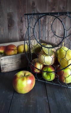 Ahşap bir masa üzerinde metal bir sepet ve elma ve armut ile bir kutu.