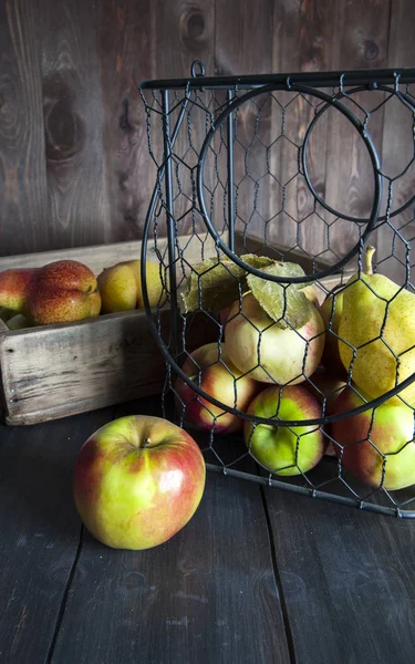 Ahşap bir masa üzerinde metal bir sepet ve elma ve armut ile bir kutu.