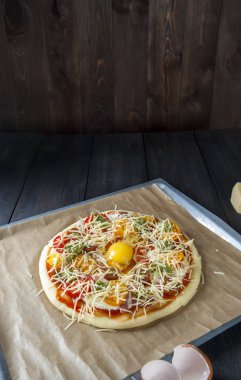 Fırın kağıdı ile kaplı bir fırın tepsisine siyah ahşap bir masa üzerinde pişirme için hazırlanan bir pizza yatıyor.