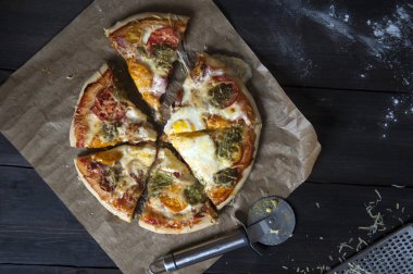Siyah ahşap bir masa üzerinde bir fırın kağıdı üzerinde yatıyor dilimlenmiş taze pişmiş pizza, üst görünümü. Yakında bir pizza bıçağı ve rende yatıyor.
