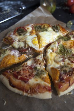 Fırın kağıdının üzerinde yatan taze pişmiş dilimlenmiş pizzanın yakın çekim. Arka planda bir rende ve pesto ile bir kavanoz görünür.