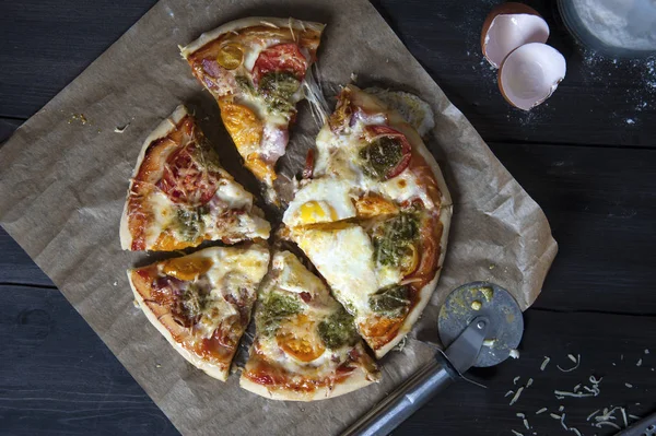 Siyah ahşap bir masa üzerinde bir fırın kağıdı üzerinde yatıyor dilimlenmiş taze pişmiş pizza, üst görünümü. Yakında bir pizza bıçağı ve yumurta kabuğu yatıyor.