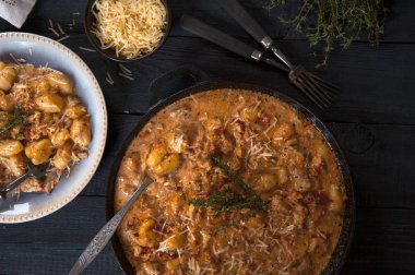 Taze hazırlanmış gnocchi ile bir kızartma tavası bir krem domates sosu kekik bir sprig ile ahşap bir masa üzerinde duruyor. Yakınlarda bir porsiyon gnocchi ve bir kase rendelenmiş peynir içeren bir tabak var..
