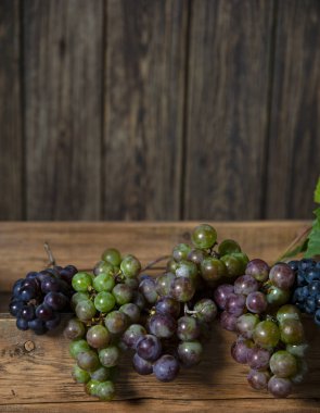 Üzüm demetleri eski bir ahşap kutunun kenarında yatıyor. Ahşap duvarın arkasında..