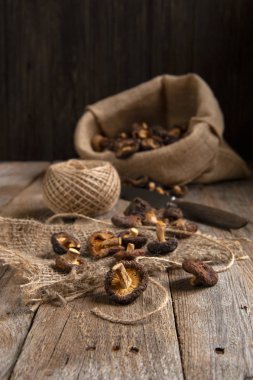 Sonbahar kurusıkı. Çiğ ahşap bir masa üzerinde bir torba kurutulmuş mantar, bir top jüt kablosu ve bir bıçak yatıyor. Mantarlar masada uyandı. Arka planda koyu tahta bir duvar var..